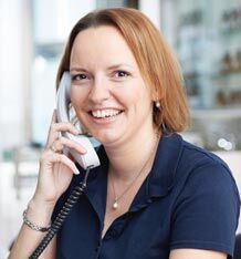 Eine lächelnde Frau in einem blauen Hemd telefoniert in einem modernen Büro.