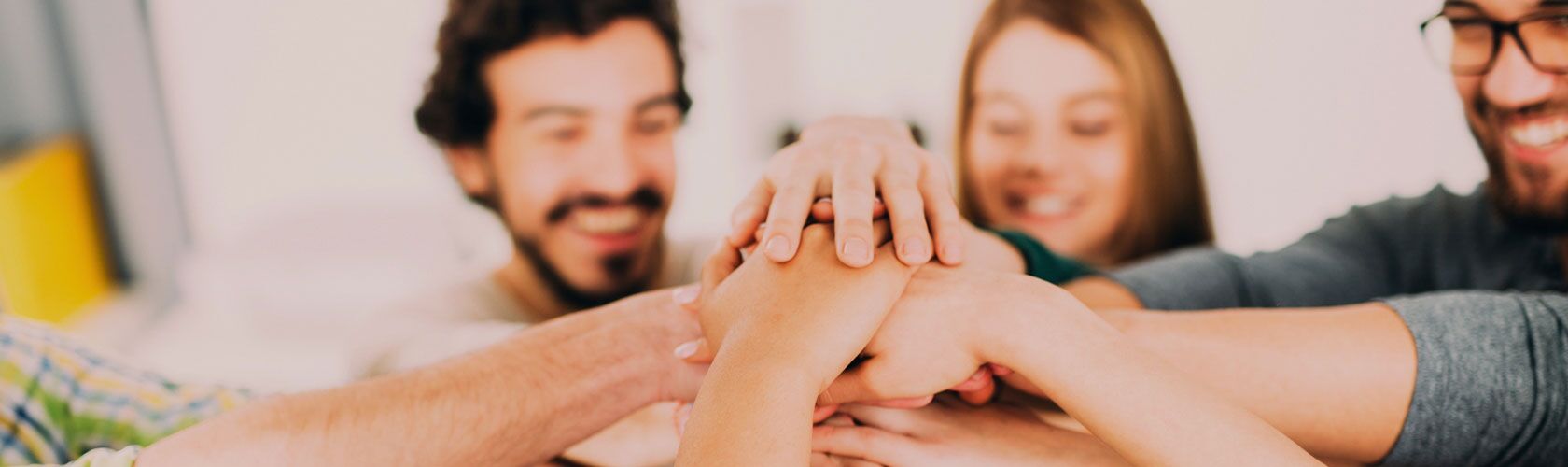 Ein Team von Menschen legt lächelnd die Hände übereinander, um Zusammenarbeit und Teamgeist zu symbolisieren.